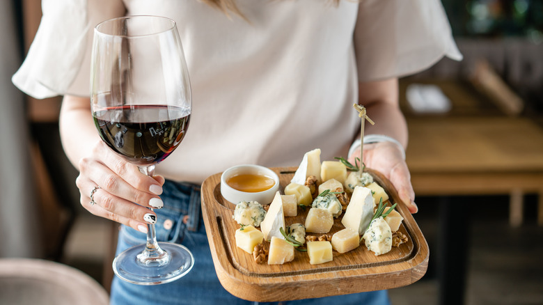 Woman holding cheese board and red wine