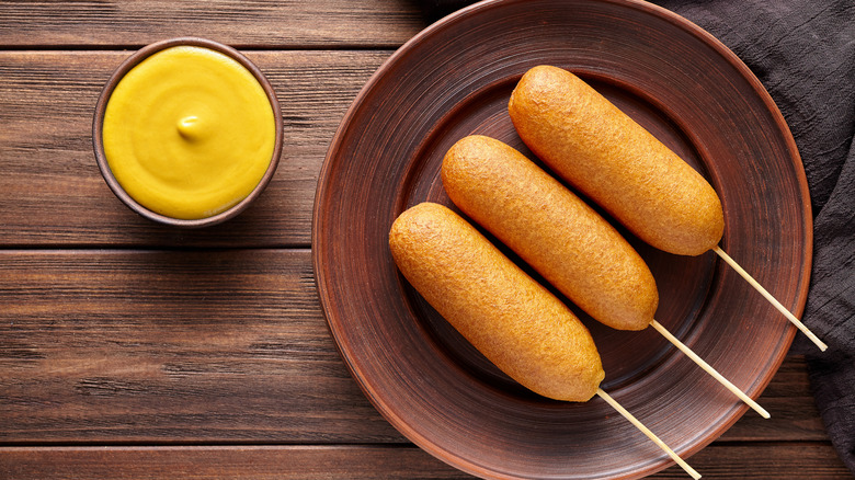 Corn dogs on plate alongside mustard