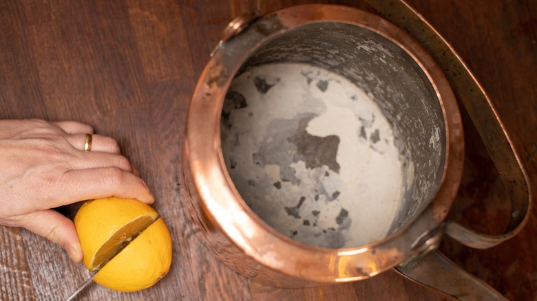 person cutting lemon beside dirty kettle