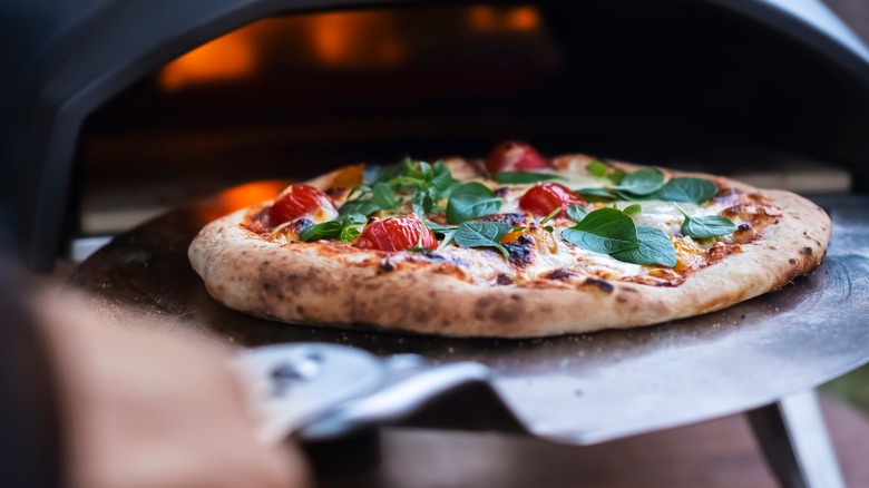 Person sliding pizza into pizza oven