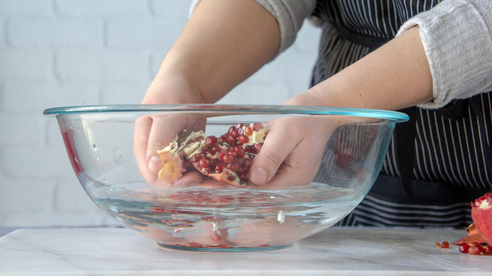 hands working arils out of the pomegranate into a bowl of water