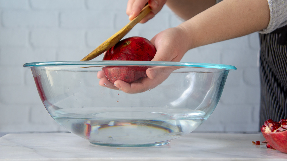 half a pomegranate being smacked with a wooden spoon over a bowl of water