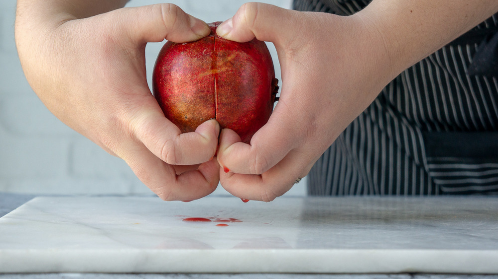 fingers digging into a sliced pomegranate