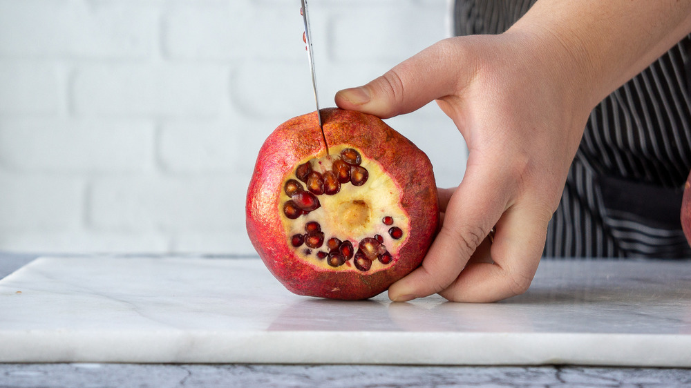 a pomegranate with the top cut off and a cut being made along the side