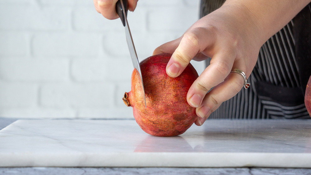 a knife slicing the top off of a pomegranate