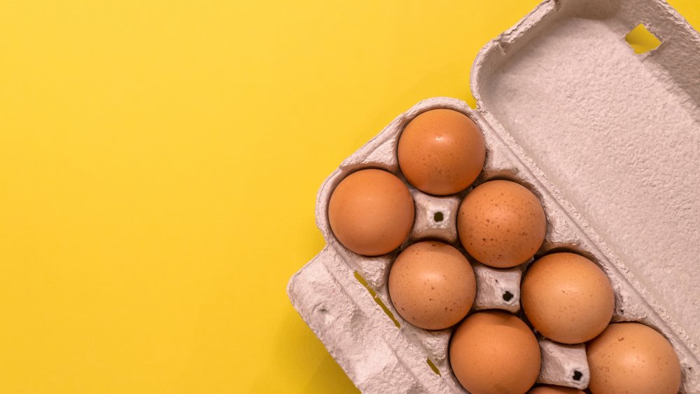 carton of brown eggs on yellow background