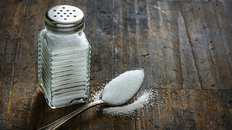 Salt shaker and spoon full of salt on wood table