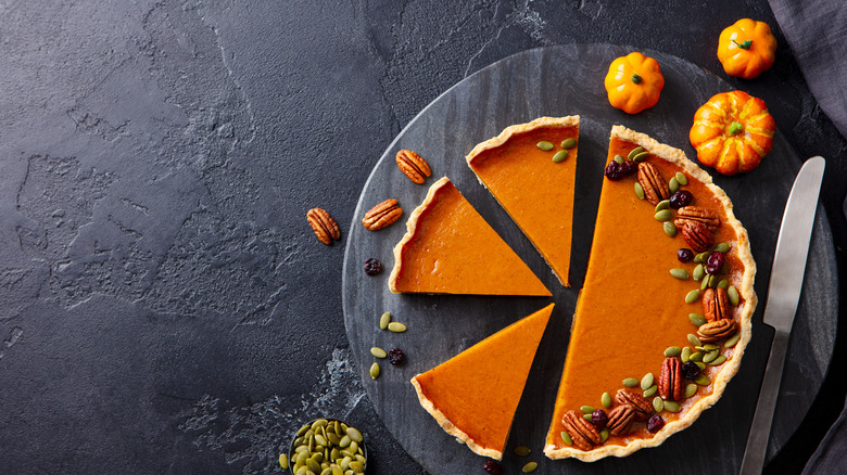 whole pumpkin pie sliced into individual servings and topped with pecans and pumpkin seeds