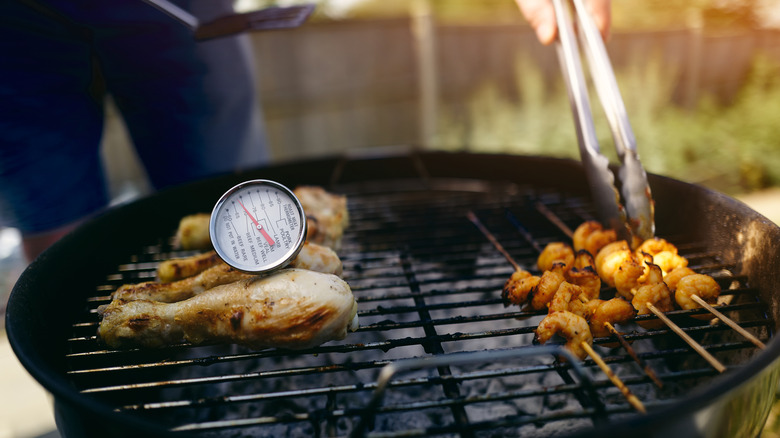 meat thermometer atop chicken drumsticks on grill