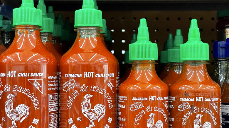 Bottles of sriracha hot sauce lined up on shelf.