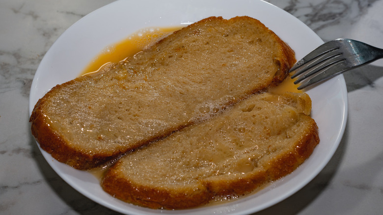 two slices of bread soaking in egg custard on plate with fork