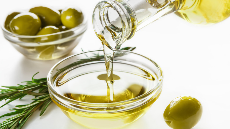 olive oil being poured and green olives in a bowl with herbs