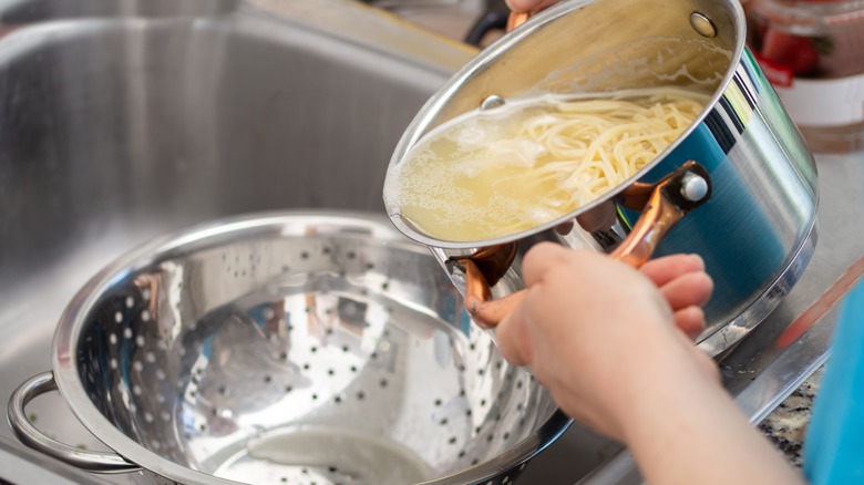 person draining pasta into colander 