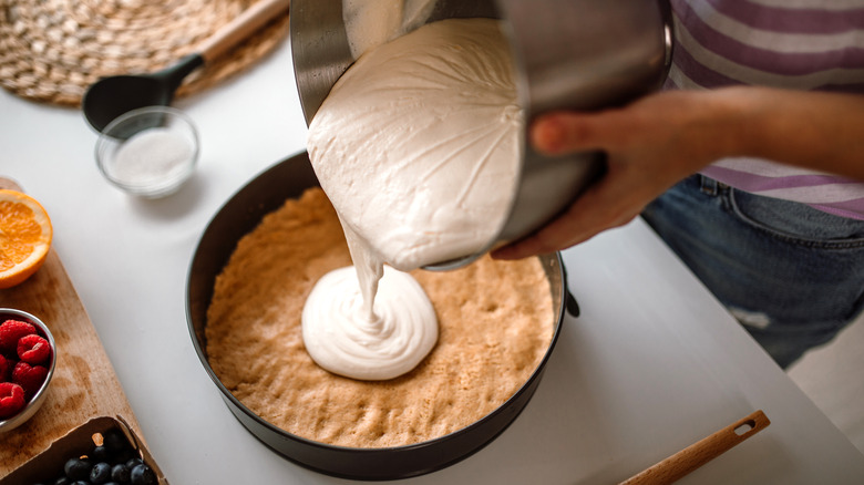 Person pouring cheesecake filling into pre-baked crust