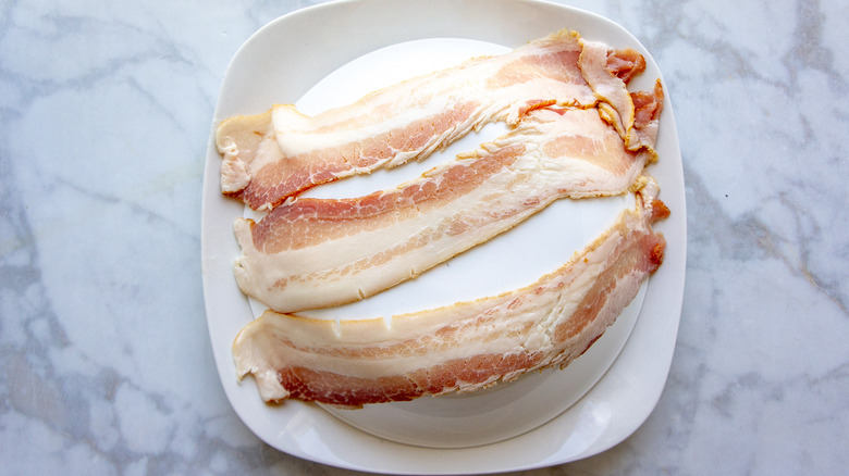 Raw bacon draped over a bowl and plate