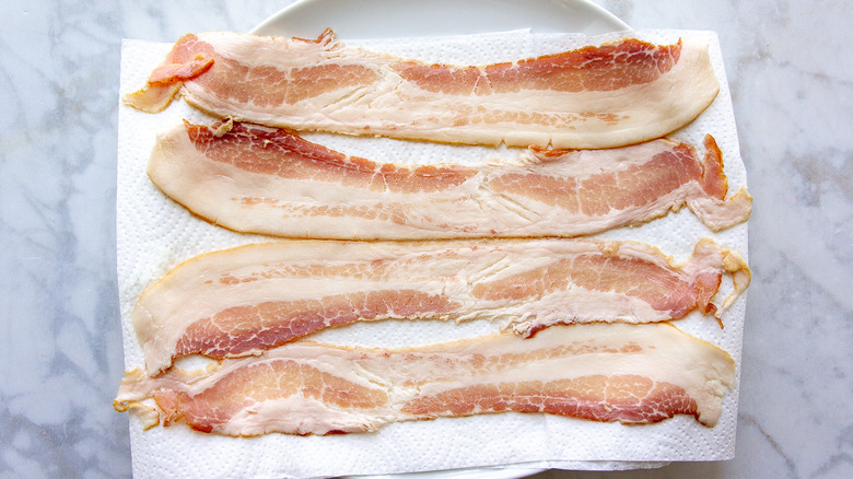 raw bacon slices on a paper towel lined plate