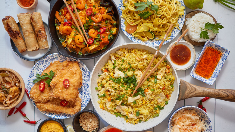 thai dishes, egg rolls, noodles, and rice all laid out and surrounded by various spices and sauces