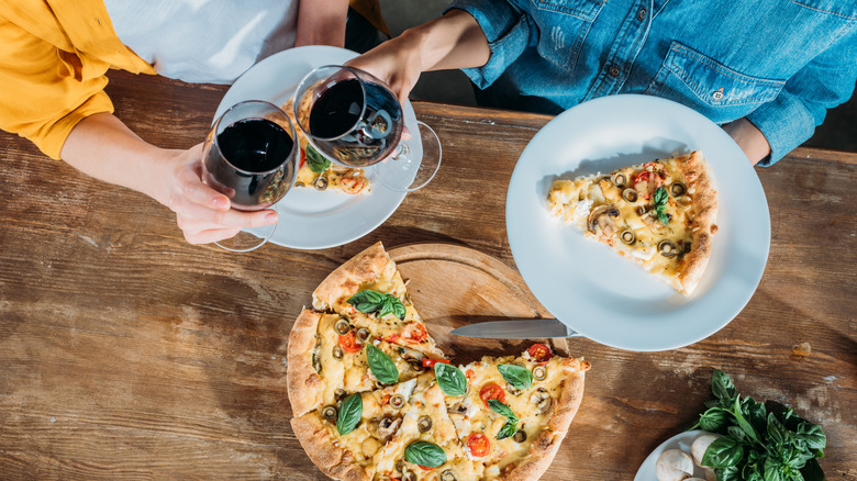 hands holding wine with pizza