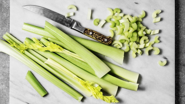 Celery stalks on white cutting board with knife