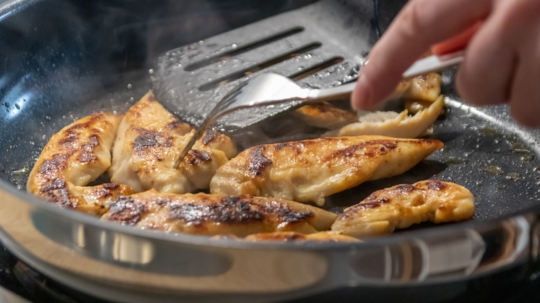 person cooking chicken in pan