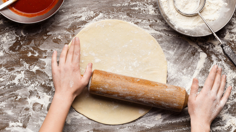 person rolling out pizza dough