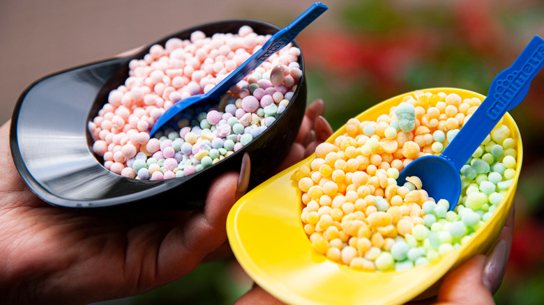 Hands holding two cups of Dippin' Dots ice cream with blue spoons.