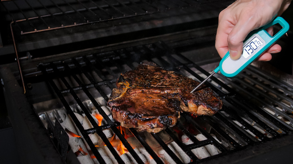 Man sticking meat thermometer into meat on grill