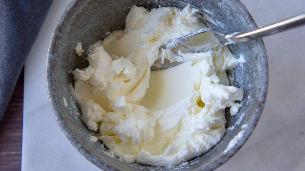 a grey bowl with cream cheese mashed in it with a knife