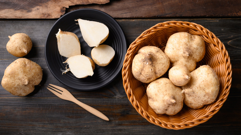 Fresh sliced jicama on black plate alongside basket of whole jicama