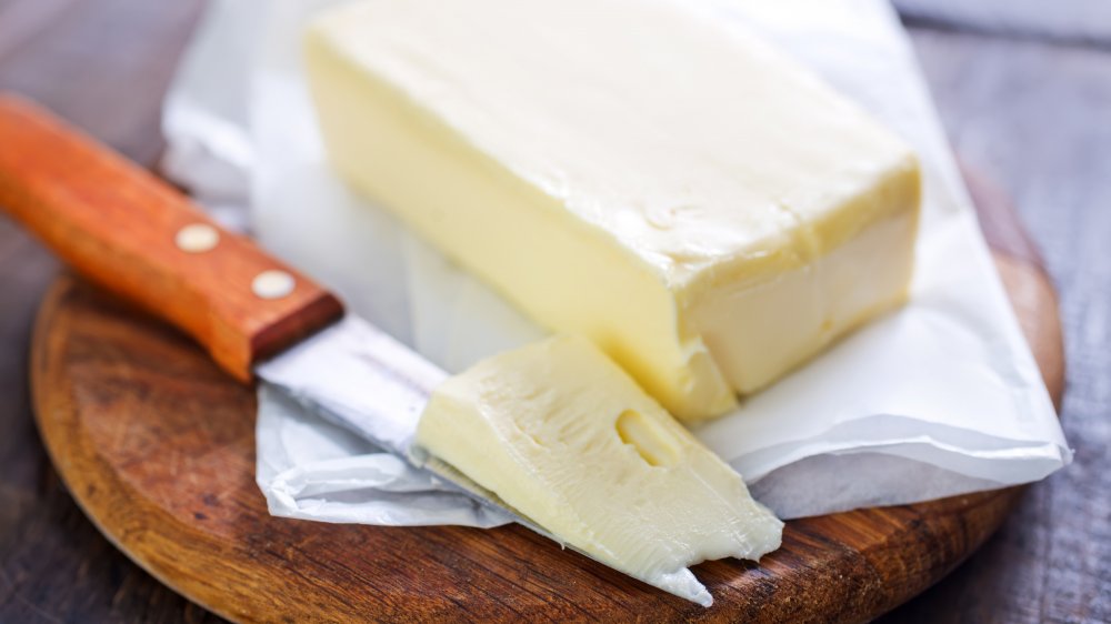 stick of butter with butter knife on a wooden cutting board