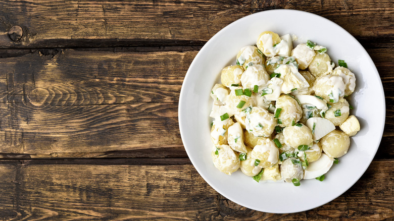 Creamy potato salad with scallions in a white bowl