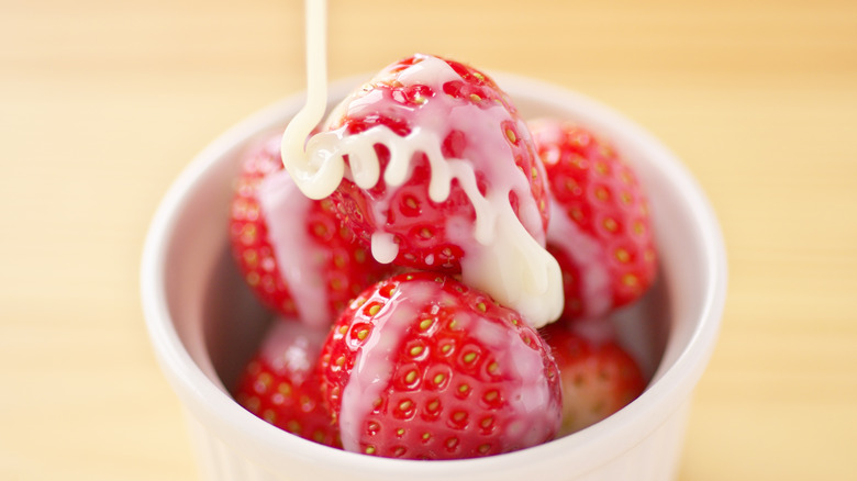 Evaporated milk drizzling over strawberries