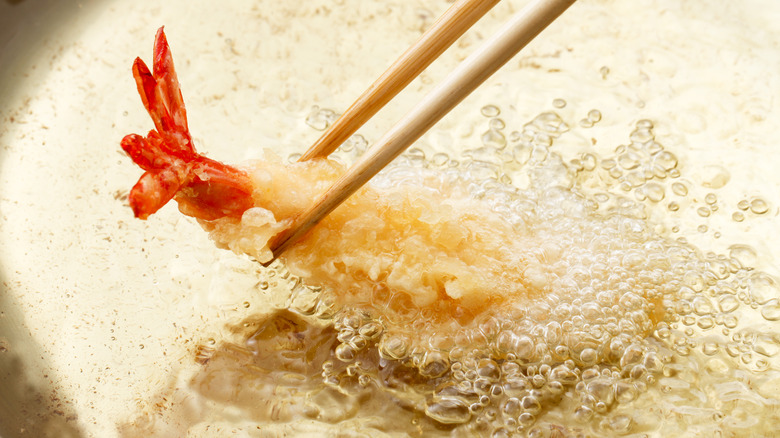 chopsticks holding shrimp tempura in oil