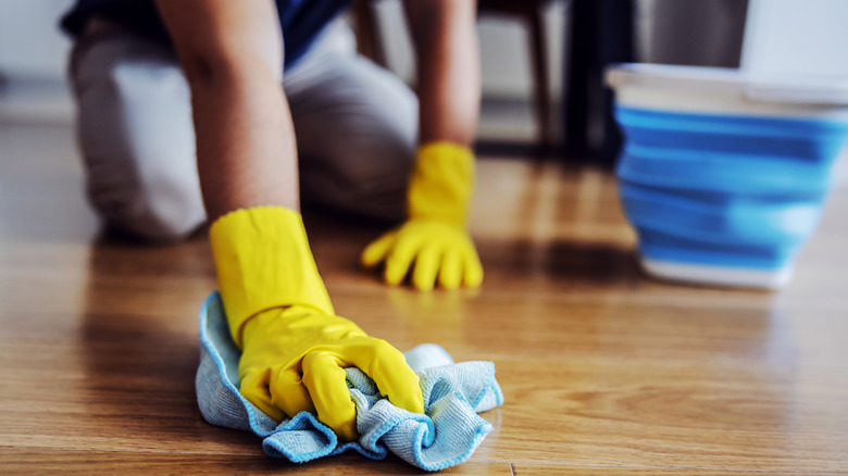 Hands in yellow gloves cleaning a wood floor