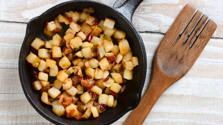 fried potatoes on a cast iron skillet beside a wooden spoon