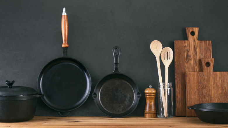cast iron skillets, wooden spoons and chopping boards on display against a black backgrouund
