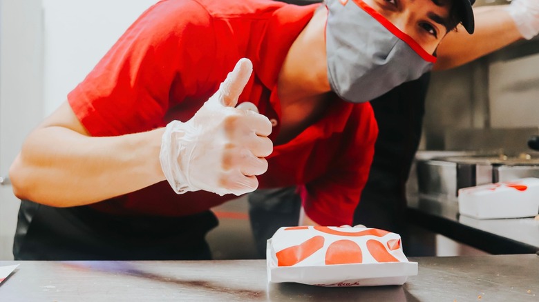 Chuick-fil-a employee wearing mask holds sandwich