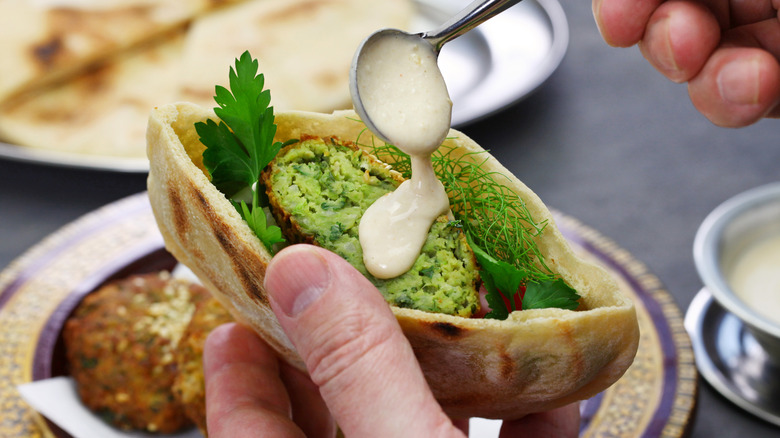 drizzling tahini over taameya in pita