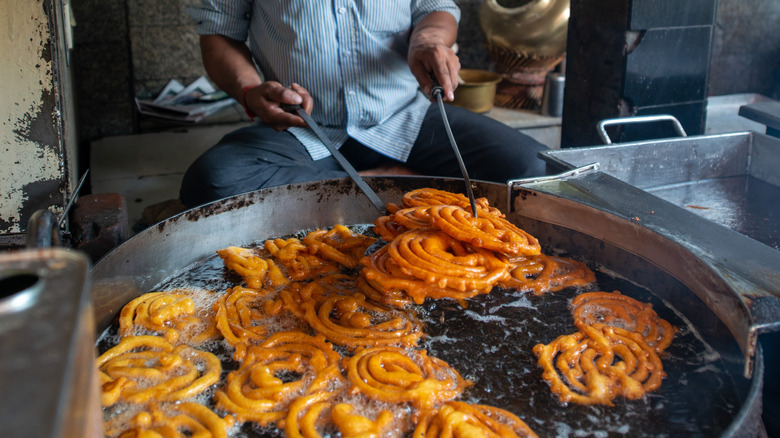 A street vendor fries jalebi in a big pot full of oil