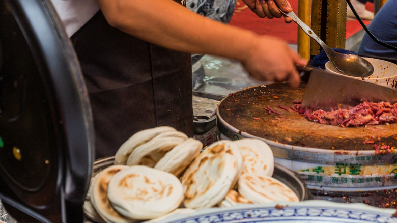 A street vendor chops meat for rou jia mo