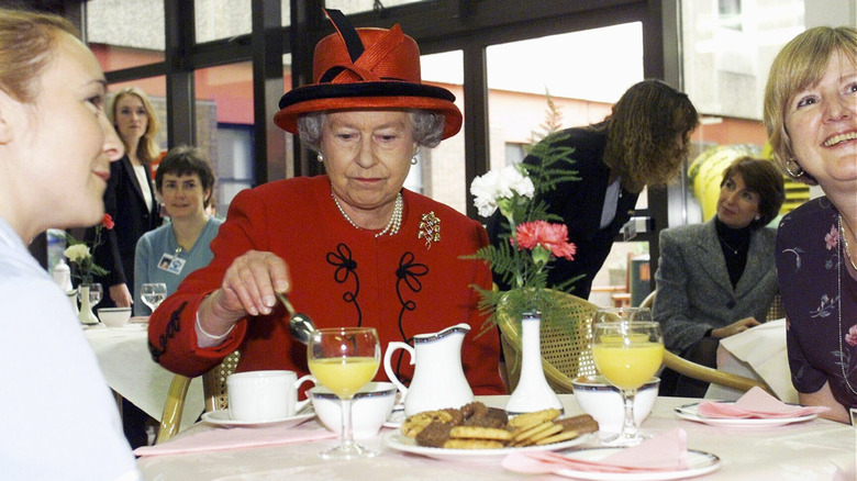 Queen Elizabeth in a red hat and jacket enjoying tea