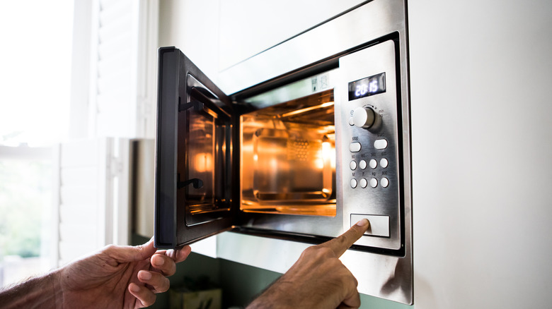 Hand pushing button on a wall-mounted microwave