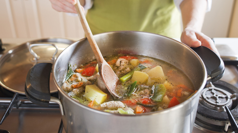 adding potatoes in pot of soup