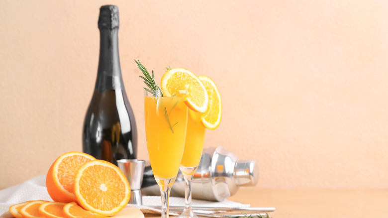 mimosas with oranges, cocktail shaker, and bottle on table