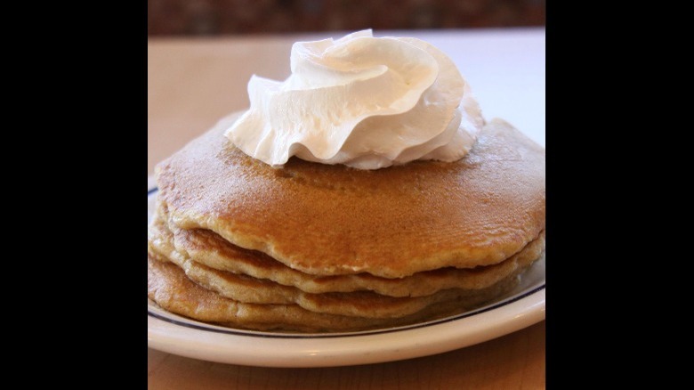 stack of four pumpkin pancakes with whipped cream