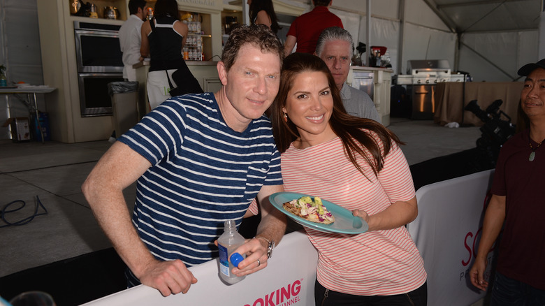Bobby Flay poses with a woman holding a dish of food