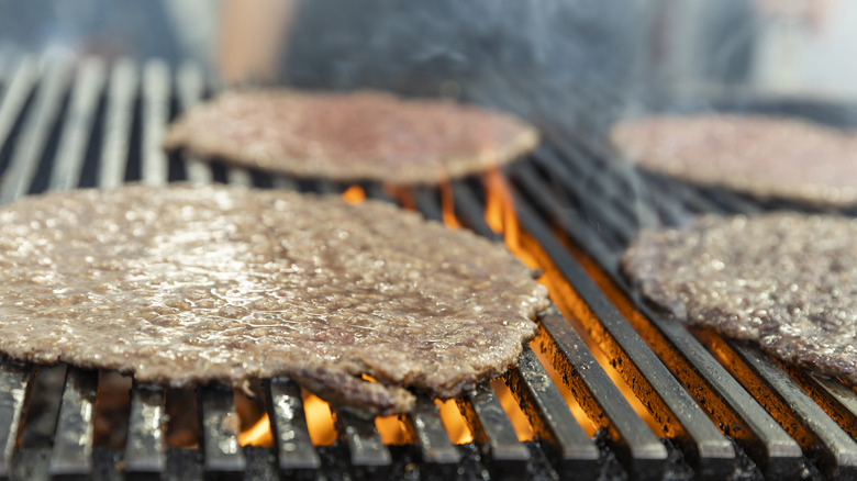 Four very thin burger patties on grill