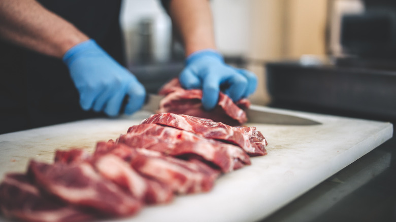 Man wearing blue gloves slicing beef