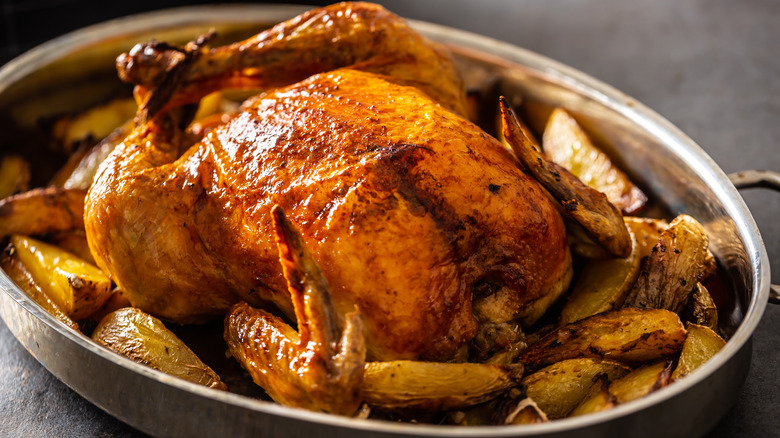 A chicken in a tray surrounded by roast potatoes