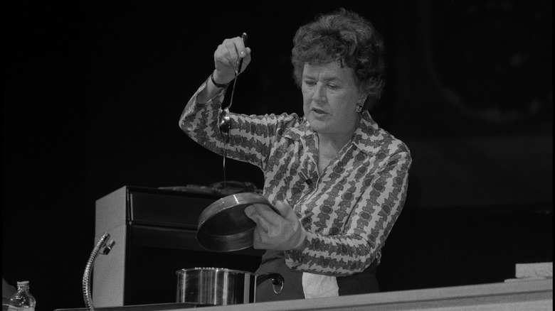 Julia Child in black and white photo holding pan top and ladle